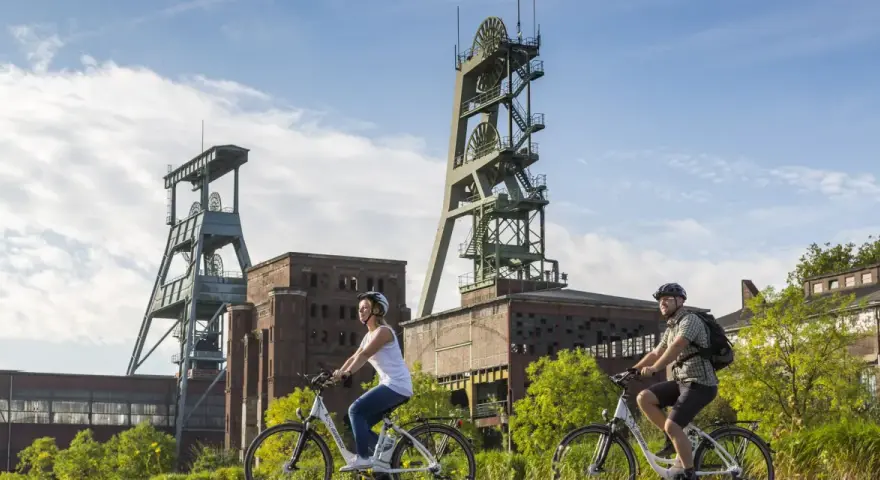 Zwei Radfahrer genießen die Aussicht auf die beeindruckenden Fördertürme der Zeche Ewald, ein Symbol für Industriegeschichte und neuen Freizeitwert.