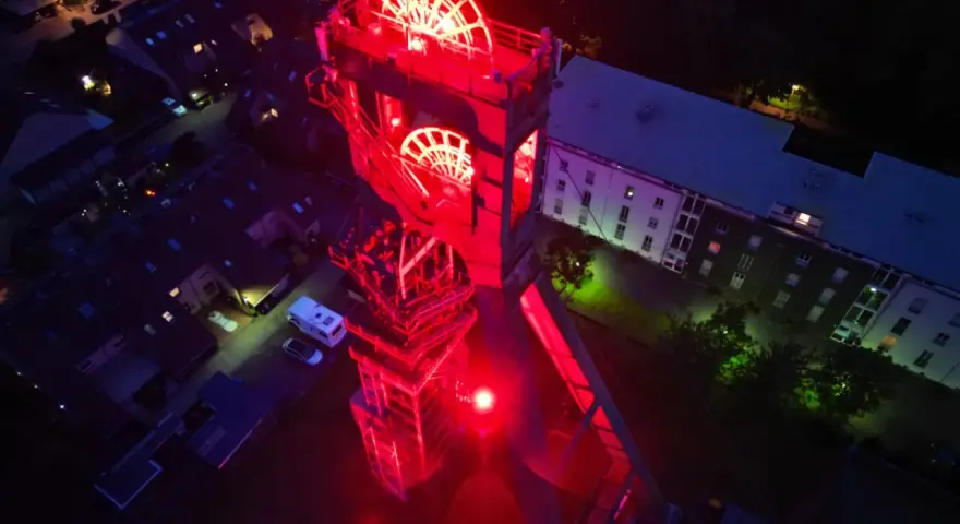 Der beleuchtete Förderturm des Erzschacht Marl erstrahlt in rotem Licht.