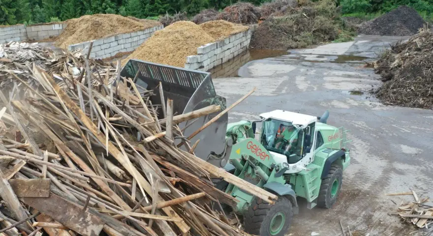 Radlader sammelt Holzreste für die Wiederverwertung. Große Haufen von recycelten Materialien sind im Hintergrund zu sehen.