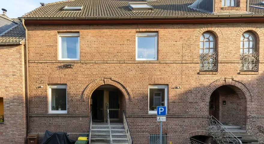 Ziegelhaus mit mehreren Fenstern und Eingängen. Ein Parkplatzschild weist auf die Lage hin, die für die Neuss Immobilienpreise relevant ist.