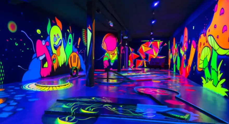 Ein leuchtendes Indoor-Minigolf-Paradies mit Neon-Wänden, die bunte Monster und Pilze zeigen.