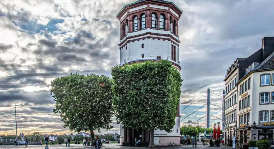 Düsseldorfer Rheinturm mit Bäumen und Gebäuden. Die Immobilienpreise in Oberbilk sind ein Thema, das viele interessiert.