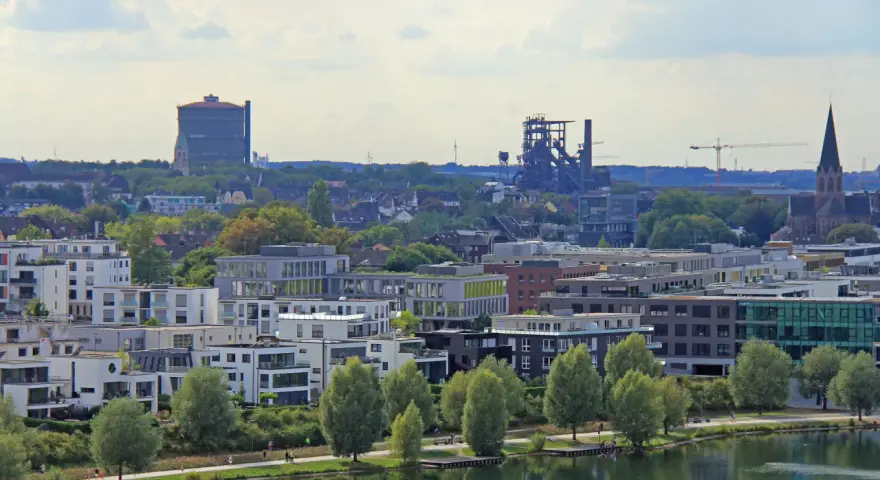 Moderne Wohngebäude am Wasser, im Hintergrund Industriedenkmäler und eine Kirche. Der Wohnungsmarkt Dortmund zeigt sich hier von seiner modernen Seite.