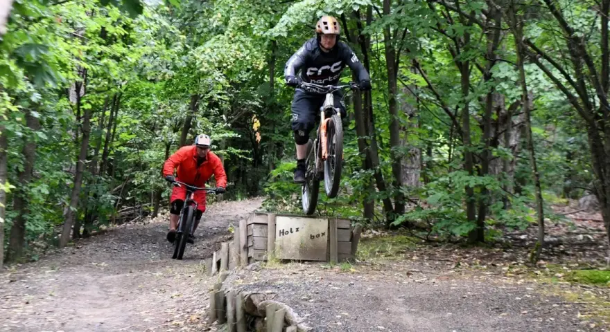 Zwei Mountainbiker springen über die Holzbox auf dem Halde Hoppenbruch Trail.