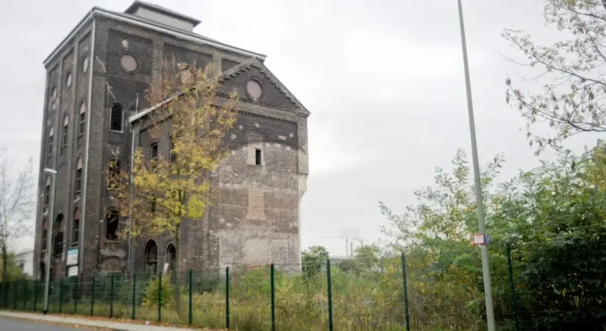 Ein verlassener Malakowturm aus dunklem Backstein, umgeben von Bäumen im Herbstlaub.