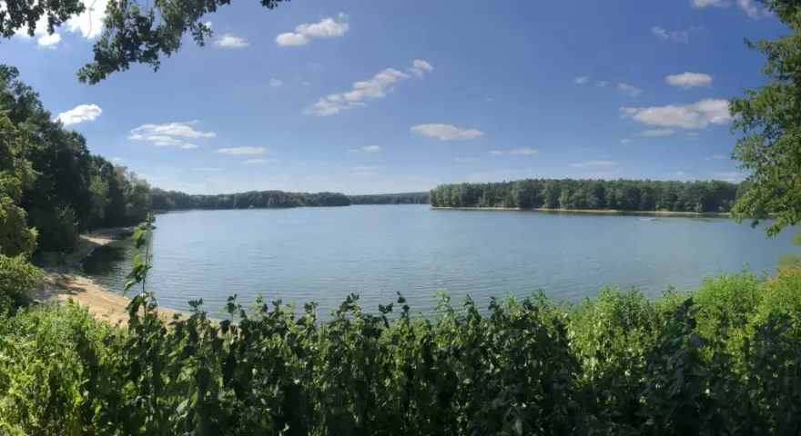 Ein ruhiger Tag am Hullerner Stausee. Grüne Bäume säumen das Ufer, das Wasser glitzert unter blauem Himmel mit weißen Wolken.