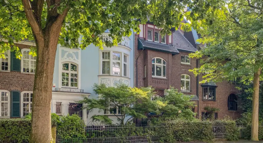Schöne Häuser mit Ziergiebeln und Erkerfenstern, umgeben von üppigem Grün. Ein idyllisches Bild für wohnen in Krefeld.