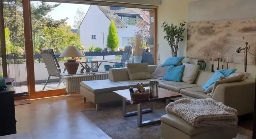 Gemütliches Wohnzimmer mit Ledercouch, Blick auf Balkon und Garten. Ein schönes Zuhause, das die Immobilienpreise in Ratingen widerspiegelt.