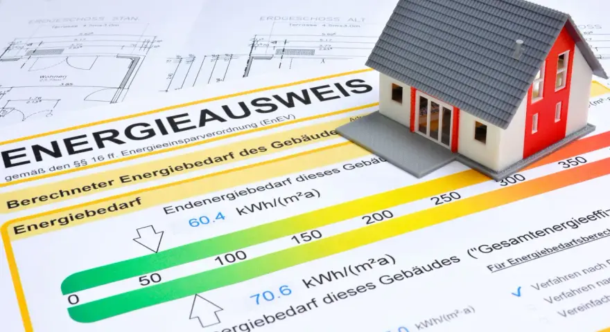 Modellhaus auf einem Energieausweis (Verbrauchsausweis oder Bedarfsausweis). Der Ausweis zeigt den Energiebedarf eines Gebäudes mit einer Skala von grün bis rot.