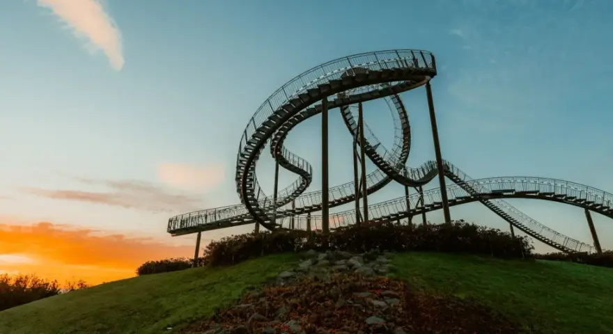 Die Achterbahn-Skulptur Tiger & Turtle auf einer Halde im Ruhrgebiet, im warmen Licht des Sonnenuntergangs.