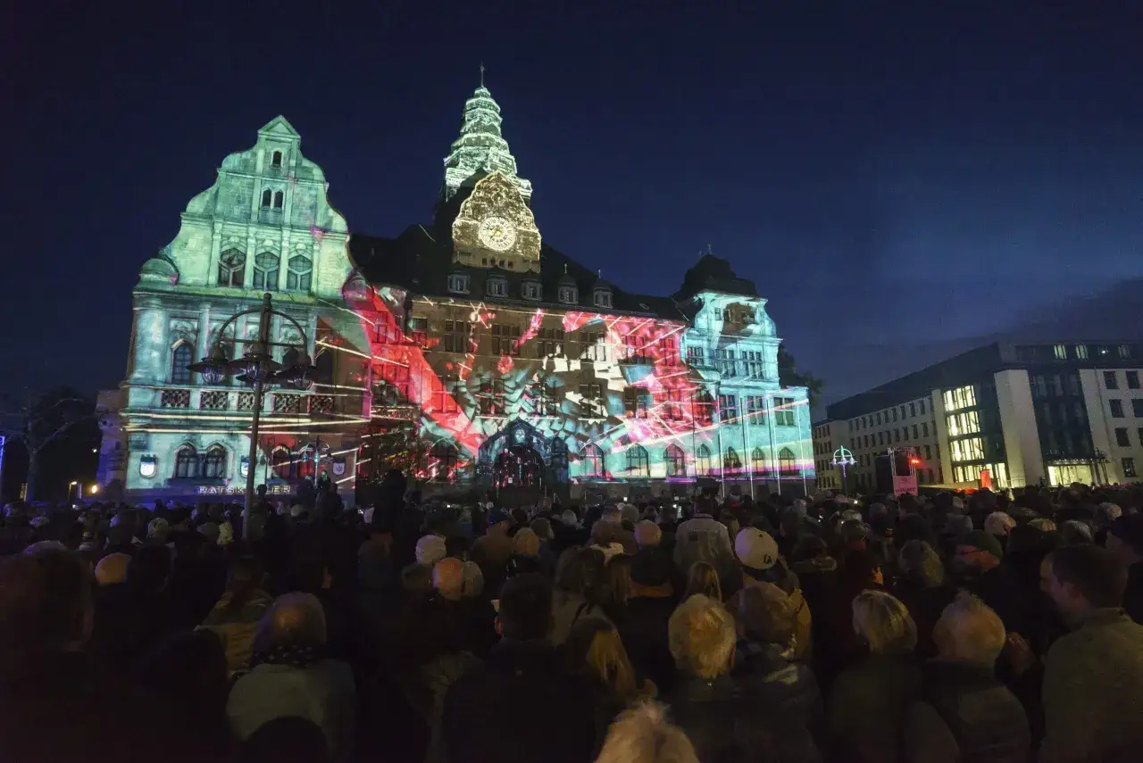 Eine Menschenmenge bestaunt eine beeindruckende Lichtprojektion auf dem Rathaus. Wann ist Recklinghausen leuchtet? Dieses Spektakel findet j&auml;hrlich statt und verwandelt die Stadt in ein magisches Lichtermeer.