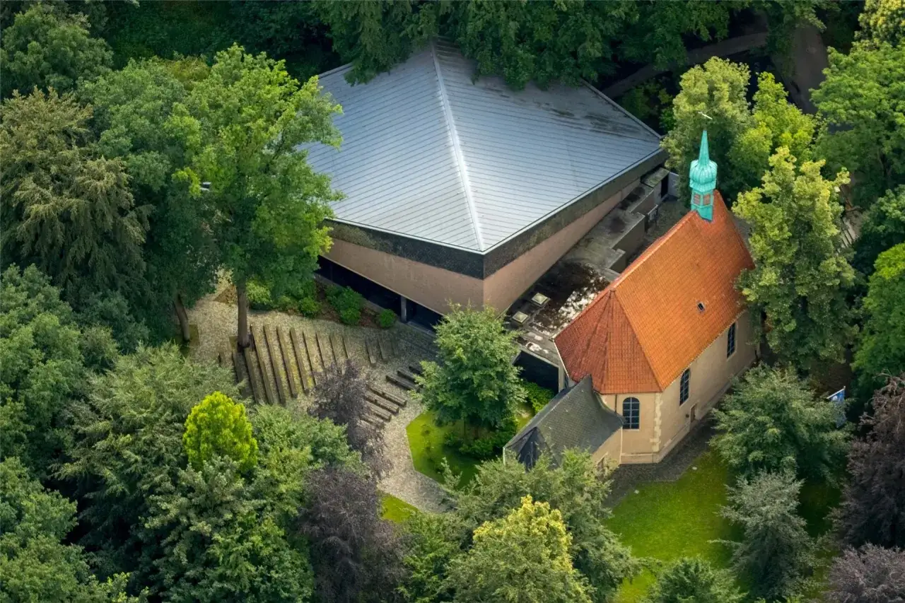 Luftaufnahme des Annabergs in Haltern, umgeben von &uuml;ppigem Gr&uuml;n. Ein moderner Bau mit Pyramiden-Dach und eine traditionelle Kirche mit Ziegeldach sind zu sehen.