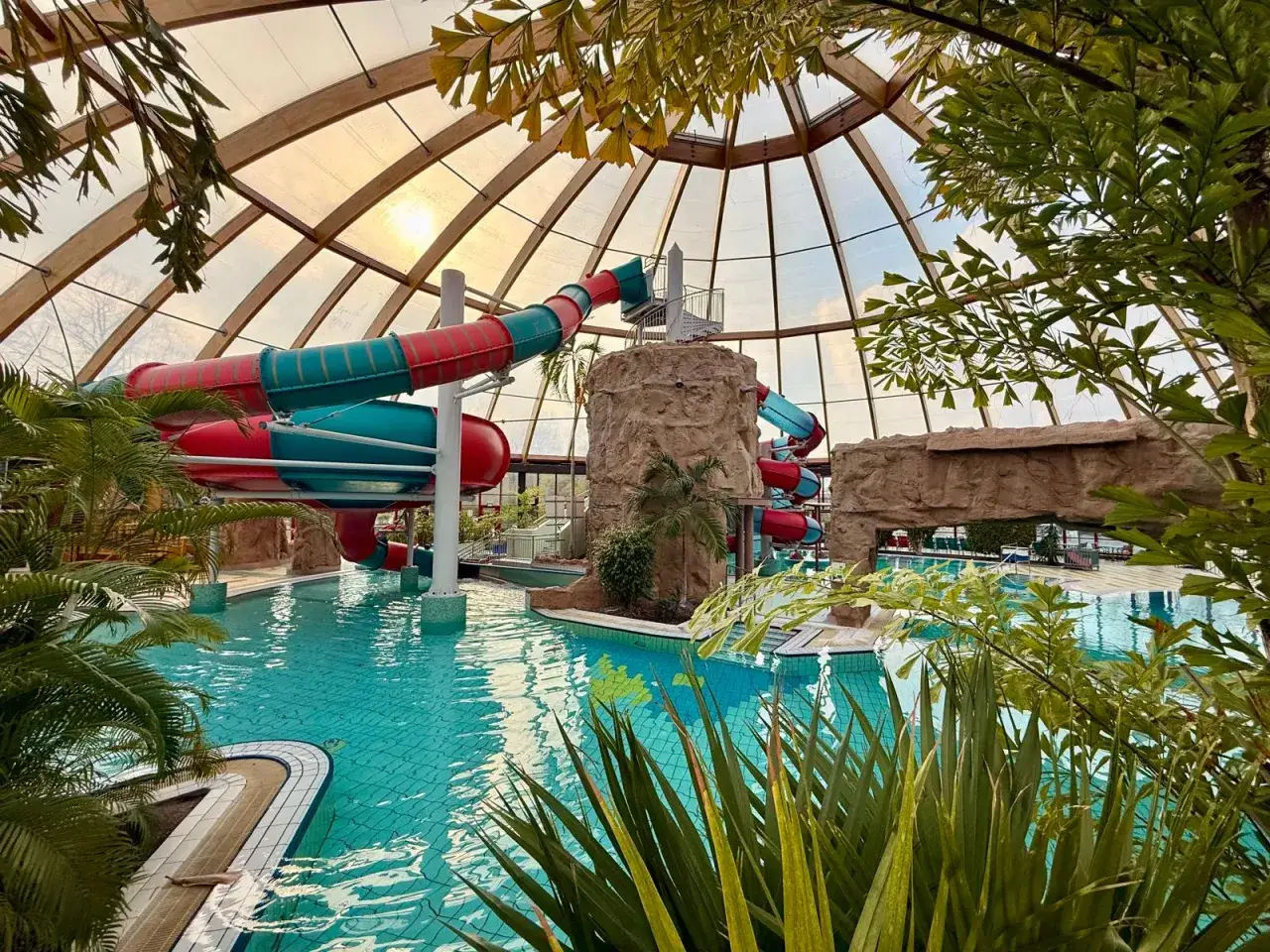 Buntes Rutschenparadies im Dorsten Freibad unter einem Glasdach, mit Palmen und Felsen.