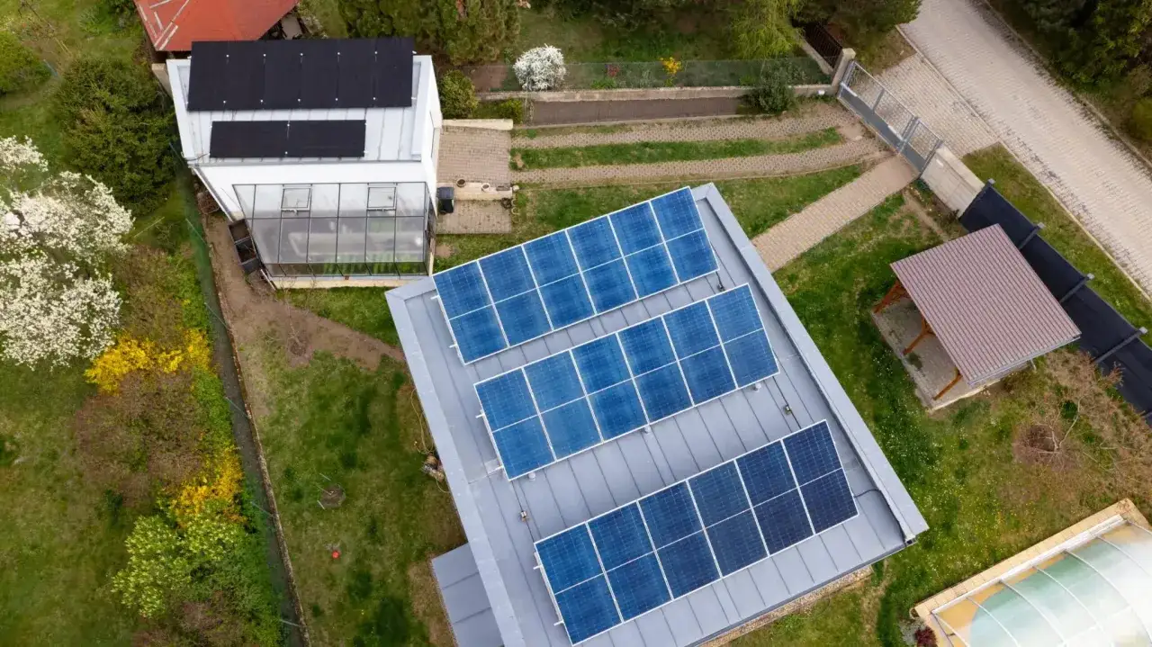 Ein selbstversorger autarkes Haus mit Solaranlagen auf dem Dach und einem Gew&auml;chshaus. Gr&uuml;ne Wiesen und bl&uuml;hende B&auml;ume umgeben das Anwesen.