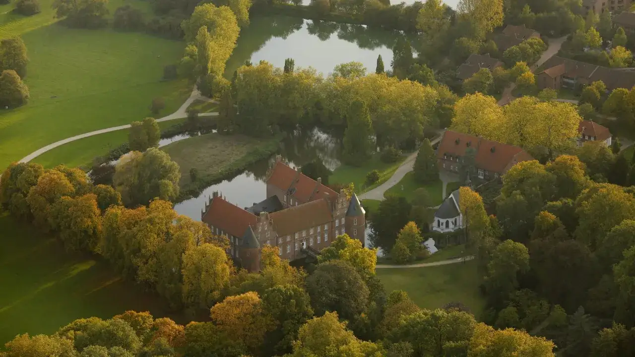 Luftaufnahme des Schlossparks Herten mit Wassergraben, Schloss und herbstlichen Bäumen.