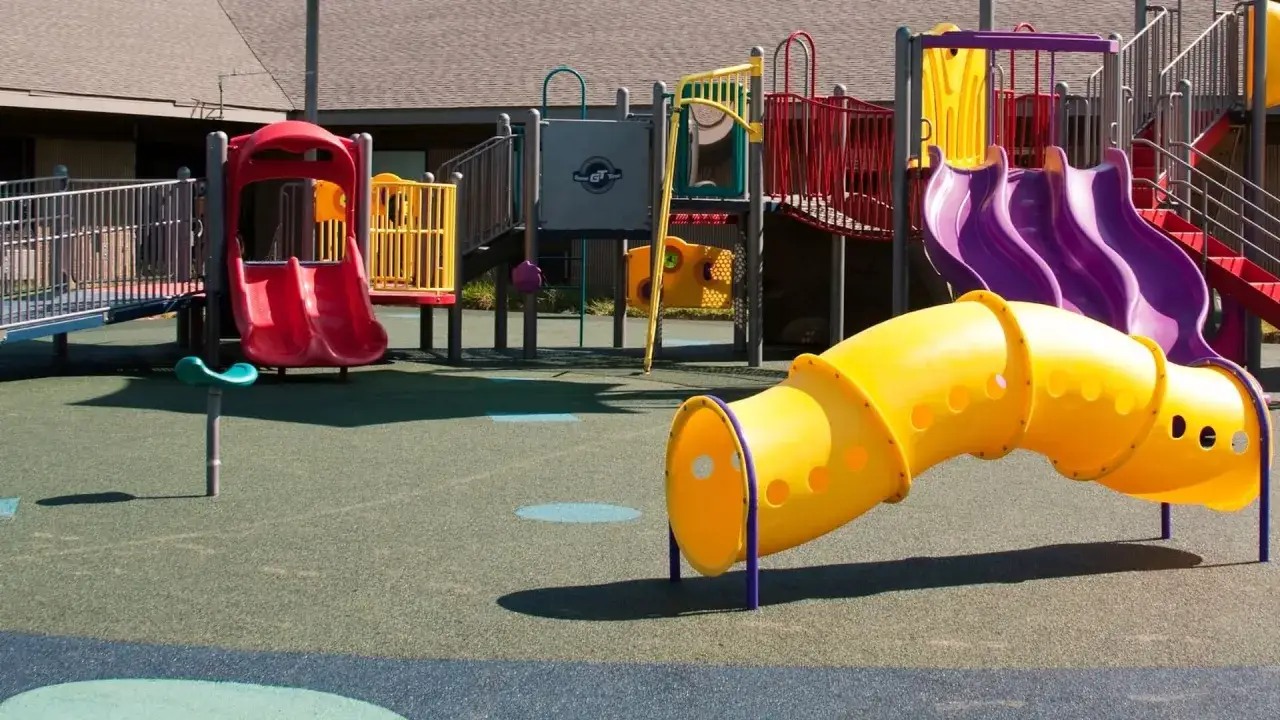 Bunter Spielplatz mit Rutschen, Tunnel und Kletterger&uuml;sten. Ein gelber Tunnel schl&auml;ngelt sich &uuml;ber den weichen Boden, bereit f&uuml;r Abenteuer.
