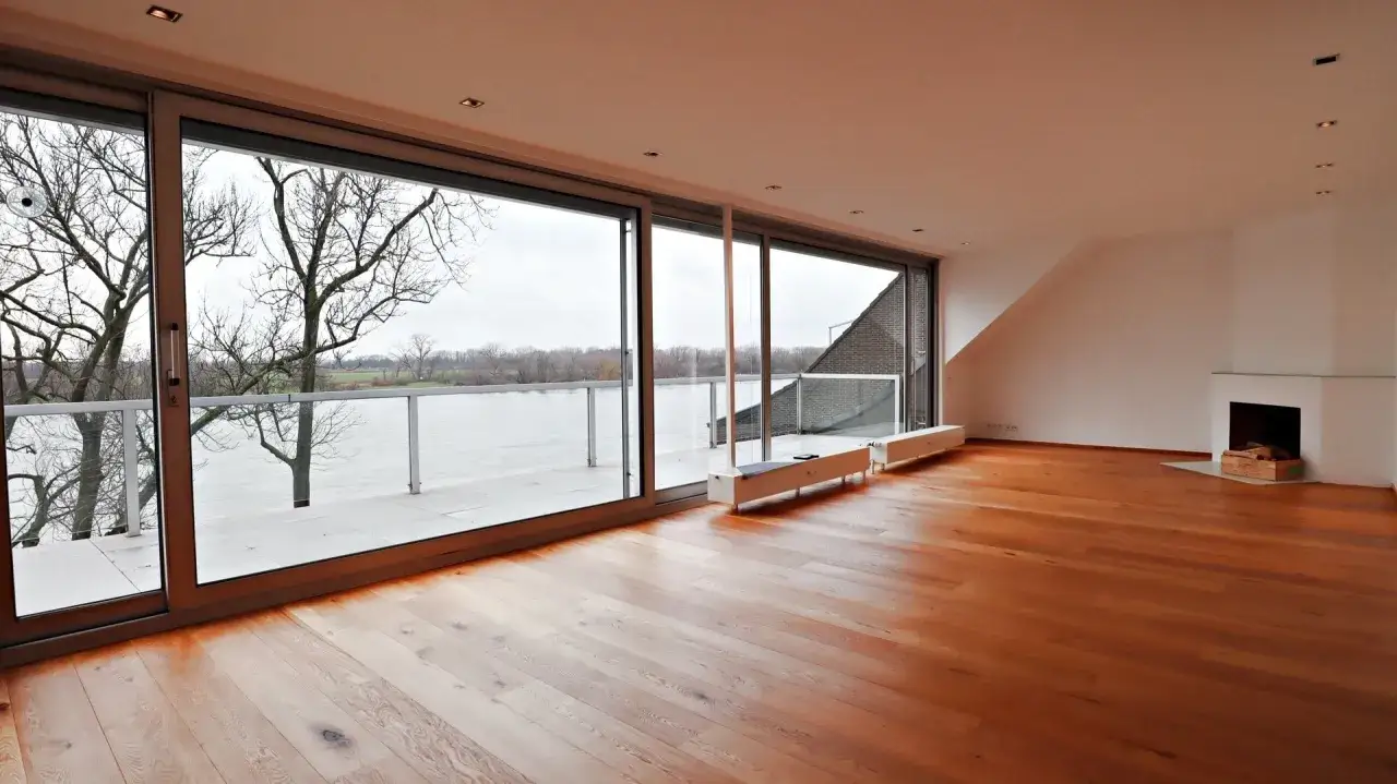 Gro&szlig;z&uuml;giges Wohnzimmer mit Parkettboden, Kamin und Panoramablick auf den Rhein. Hier k&ouml;nnte Ihre Traumimmobilie in Wittlaer liegen, die Immobilienpreise sind attraktiv.