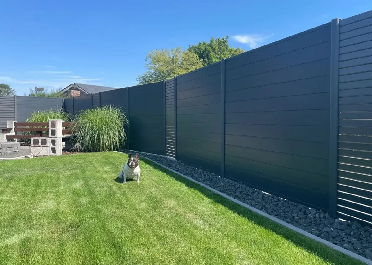 Moderner Sichtschutz im Garten mit dunkler Holzoptik. Ein kleiner Hund sitzt auf dem Rasen vor dem Zaun. Tolle Sichtschutz Garten Ideen.