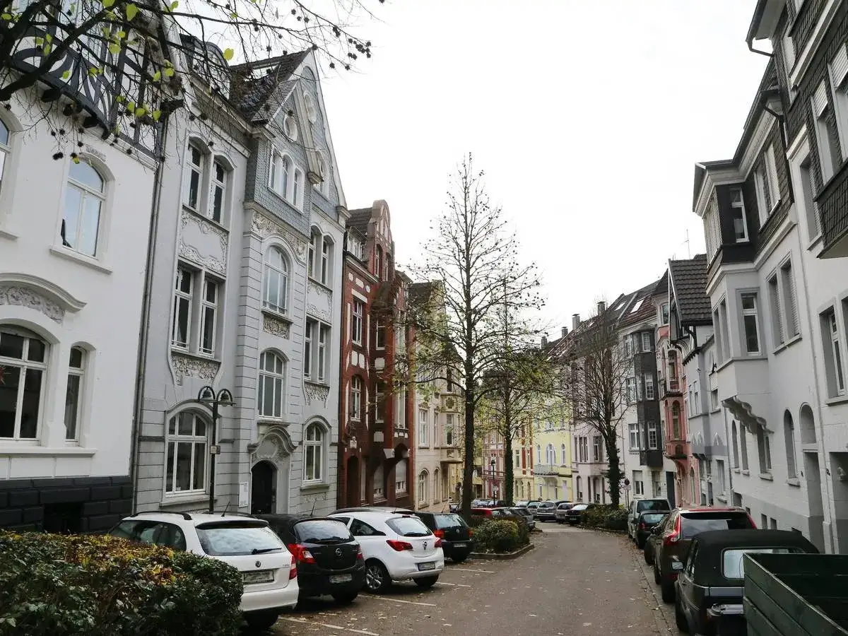 Reihenhäuser in Solingen, die einen Eindruck vom Mietspiegel vermitteln. Autos parken auf der Straße vor den bunten Fassaden.