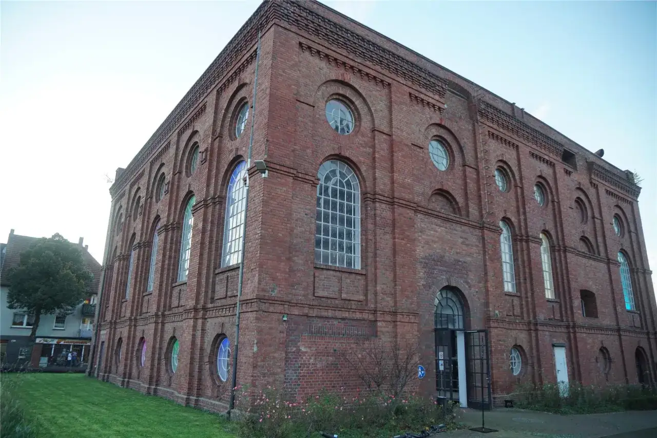 Das imposante Backsteingeb&auml;ude der Zeche Scherlbeck mit seinen vielen Rundbogenfenstern und kleinen runden Fenstern, die teils bunt beleuchtet sind.