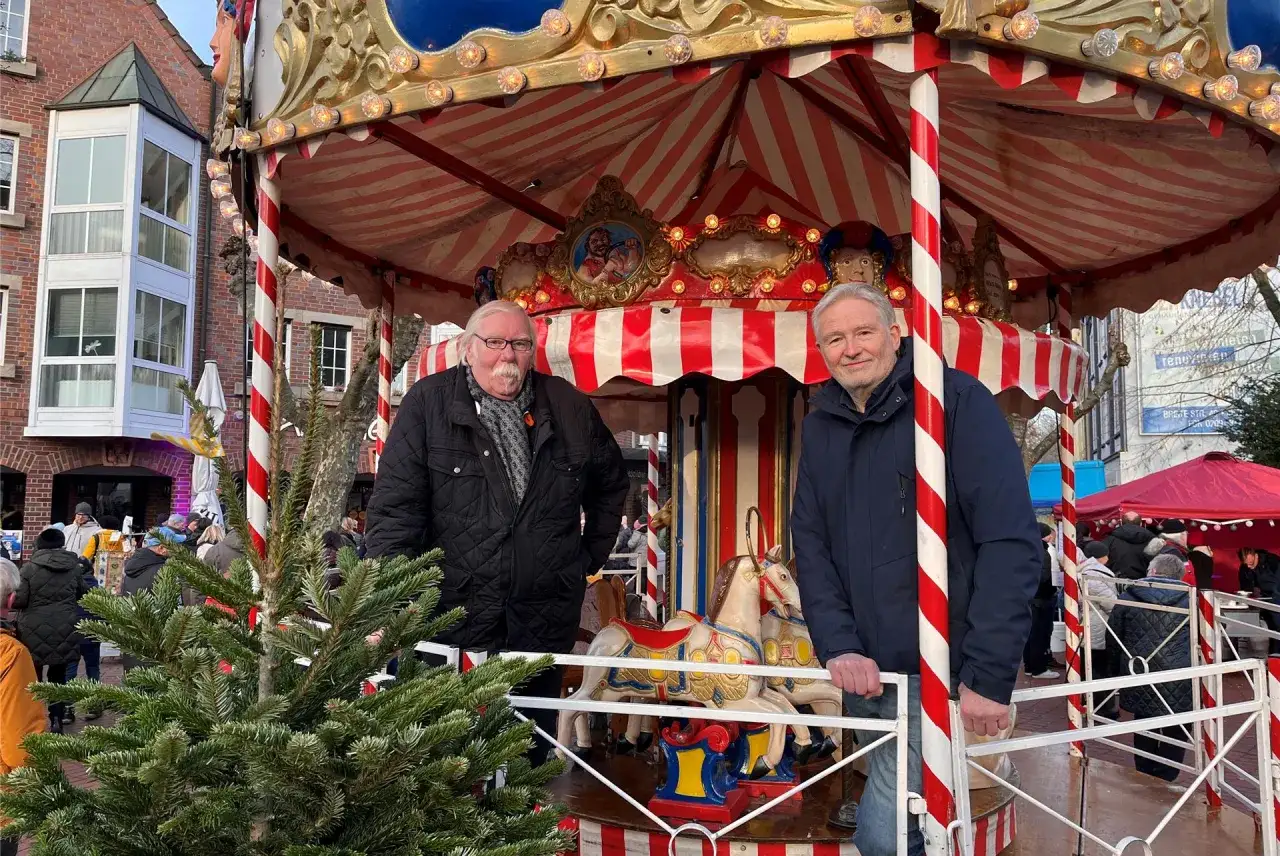 Zwei Männer stehen auf einem Karussell auf dem herten weihnachtsmarkt. Im Vordergrund steht ein Weihnachtsbaum.