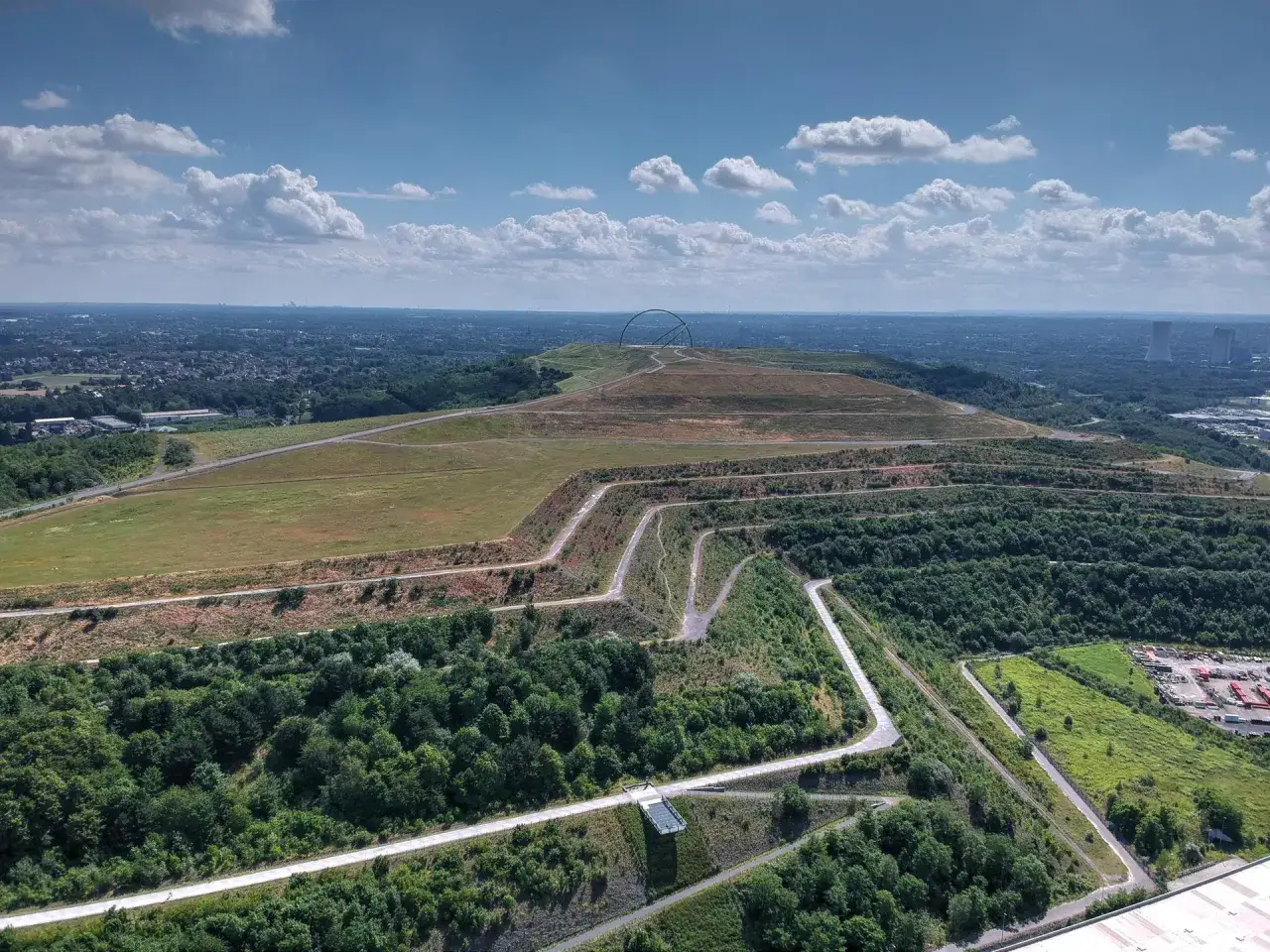 Weite Landschaft mit geschwungenen Wegen, ideal f&uuml;r eine Fahrradtour in Recklinghausen. Im Hintergrund ragt eine markante Skulptur auf.