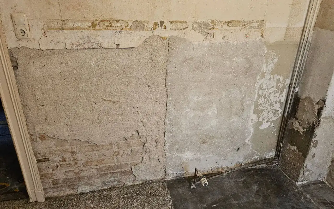Abbl&auml;tternder Putz enth&uuml;llt Ziegelmauerwerk. Die Wand zeigt Risse und Verf&auml;rbungen, die auf m&ouml;gliche Probleme hinweisen, die man bei der Suche nach asbest erkennen sollte.