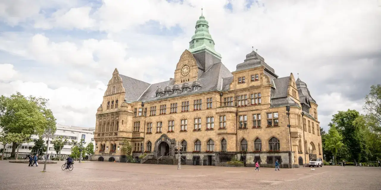 Das Rathaus am Marktplatz Recklinghausen mit seinem markanten Turm und der Sandsteinfassade. Menschen spazieren &uuml;ber den Platz.