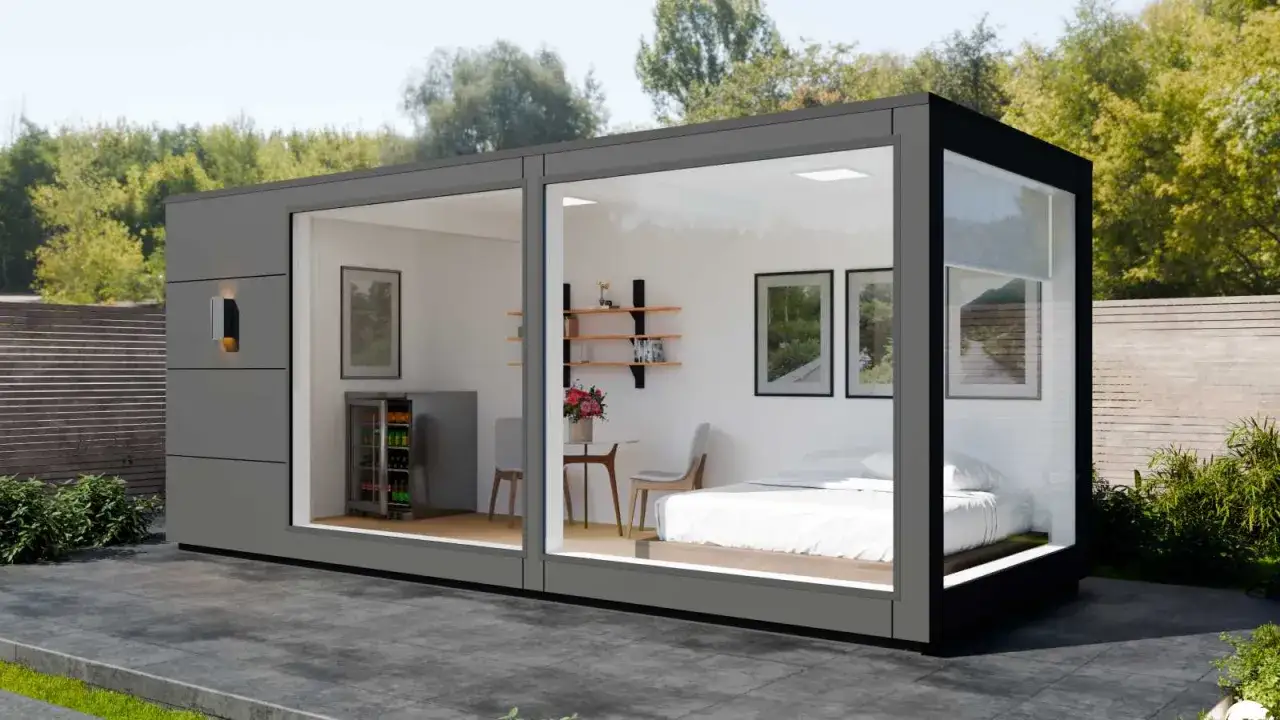 Modernes tiny house container mit Bett, K&uuml;hlschrank und Sitzbereich, umgeben von Gr&uuml;n.