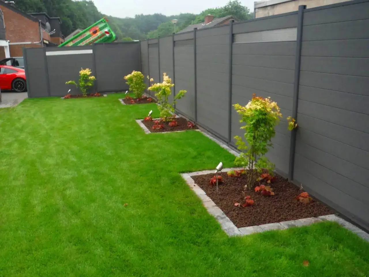 Moderne Sichtschutz-Garten-Ideen: Ein gepflegter Rasen mit jungen Bäumen und einer grauen Zaunanlage.