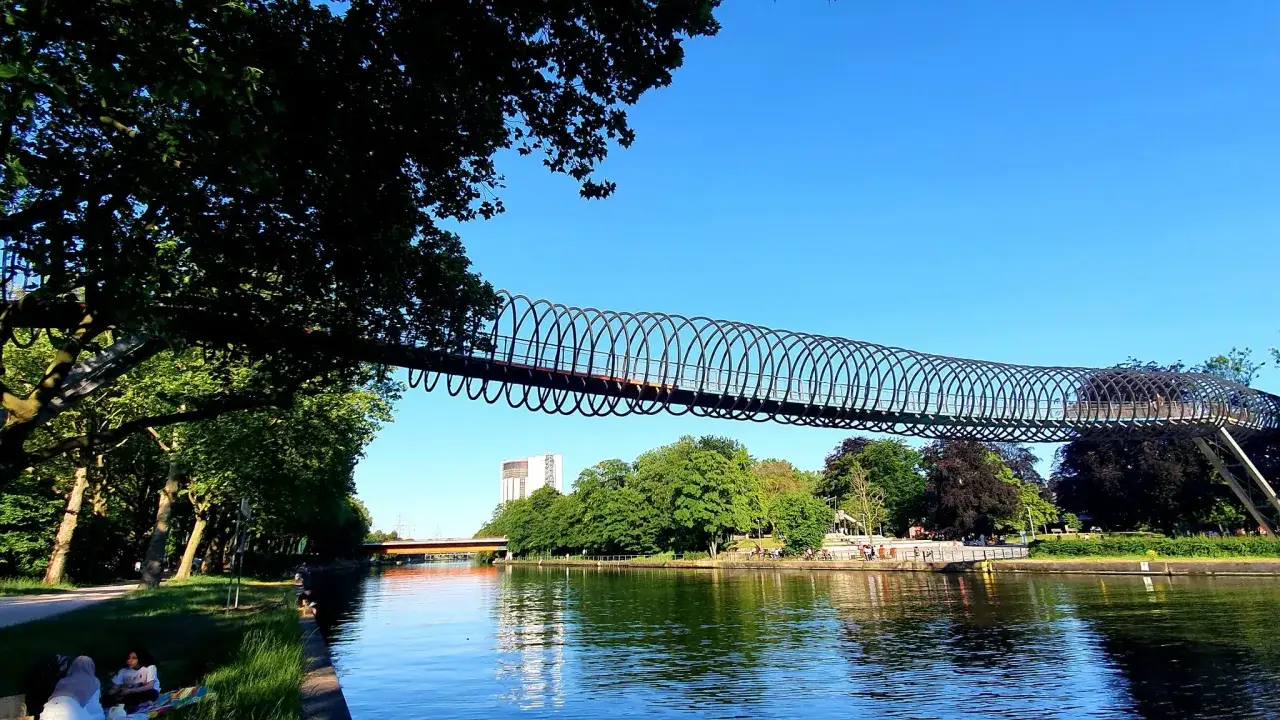 Einzigartige Spiralbr&uuml;cke &uuml;berspannt den Rhein-Herne-Kanal. Radweg l&auml;dt zum entspannten Fahren ein, w&auml;hrend Menschen am Ufer picknicken.