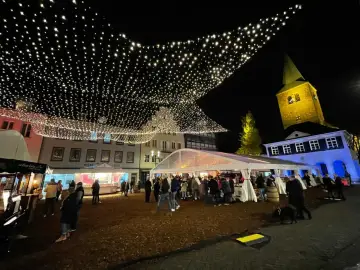Glitzernde Lichterketten schmücken den **Weihnachtsmarkt in Dorsten**. Menschen bummeln unter Zelten und vor Buden, während im Hintergrund die beleuchtete Kirche thront.