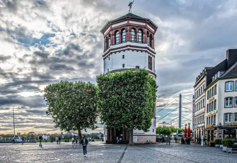 Düsseldorfer Rheinturm mit Bäumen und Gebäuden. Die Immobilienpreise in Oberbilk sind ein Thema, das viele interessiert.