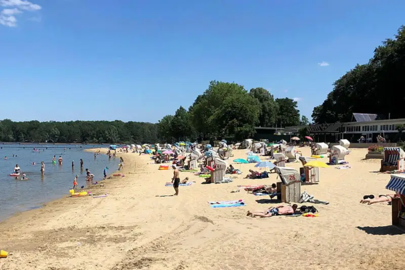 Sonniger Tag am **Haltern am See Strand** mit vielen Badegästen, Strandkörben und Bäumen im Hintergrund.